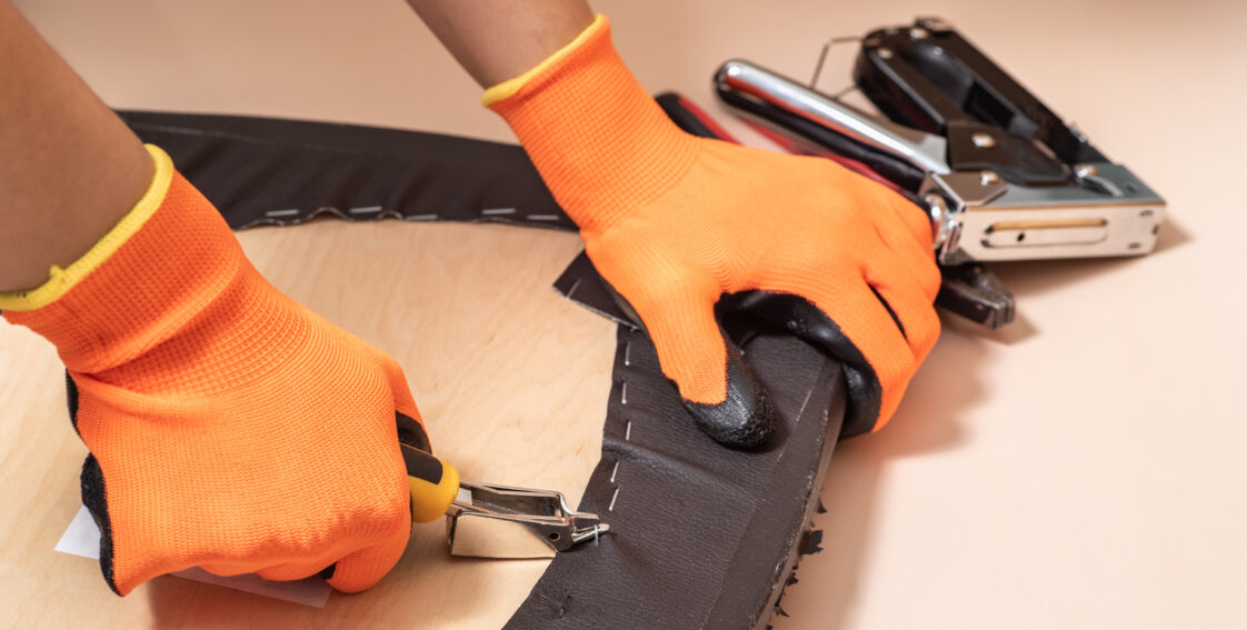 A man wears gloves and removes upholstery from a chair using a specialty tool